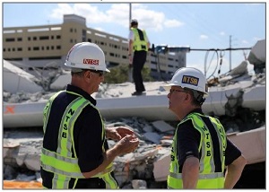 Photo shows two NTSB investigators talking in yellow vests and hardhats.