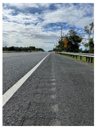 Close up of a rumble strip to the right of the lane delineation striping on the shoulder of a roadway.