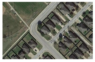This aerial photo shows a road in a residential area with a 90-degree curve.