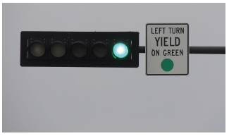 Figure 13. A picture of a 'LEFT TURN YIELD ON GREEN BALL' (MUTCD 10-12) sign on a signal mast arm adjacent to the left-turn signal head, which also shows a green ball display.