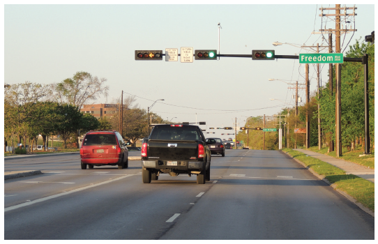 Figure 35. An image showing the approach to a signalized intersection with a mast arm-mounted signal head above each of the three approach lanes.  The signal heads above the two through lanes show a green ball, and the signal head above the left-turn lane shows an active flashing yellow arrow for permissive left turns.