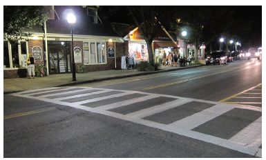 Figure 36. An image showing a ladder-style crosswalk on a two-lane street with on-street parking lanes in a shopping district at night.