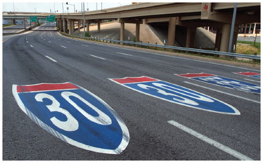 Figure 50. An picture of a section of freeway with route shield markings painted within the lanes.  The left two lanes have an I-30 shield, and the right two lanes have an I-35E shield.