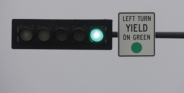 Figure 13. A picture of a 'LEFT TURN YIELD ON GREEN BALL' (MUTCD 10-12) sign on a signal mast arm adjacent to the left-turn signal head, which also shows a green ball display.