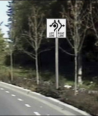 Figure 83. A picture of an approach to a roundabout with an experimental advance lane control sign superimposed on the roadside in the picture.