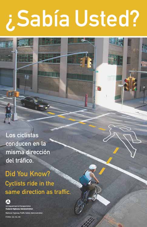 The photograph shows a cyclist riding into an intersection even though he clearly the traffic signal is red on his path. A car approaches the same intersection from the path that has a green light in the traffic signal. Dotted lines that arrive at a body outline indicate where the paths of the car and the bicyclist would meet if they continue on their present paths. The English text reads: Did you know? Cyclists ride in the same direction as traffic. The Spanish text reads:  ¿Sabía Usted? Los ciclistas conducen en la misma dirección del tráfico. 