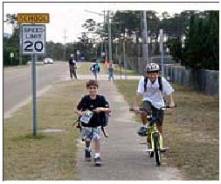 Photograph of two children going to school, one walking and one riding a bike.