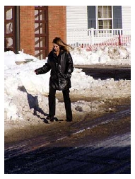 Photo of woman navigating the edge of a roadway where snow has been plowed over the pedestrian walkway.