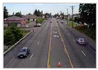 Photo of a roadway with two lanes traveling in opposite directions separated by a two-way-left-turn lane with no crosswalks or sidewalks.