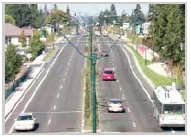 Photo of a roadway with two lanes traveling in opposite directions separated by a median and with sidewalks on either side of the road.