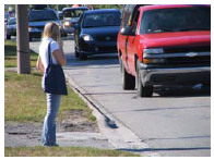 Photo a person waiting by a roadside for a break in traffic so she can cross at an unmarked location.