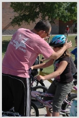 Photo of a child on a bike with a man properly placing and securing her safety helmet on her head.
