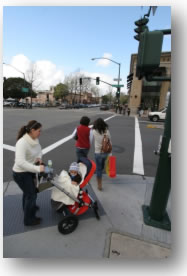 Photo of pedestrians waiting to cross the street at a signalized crossing with a traffic light.