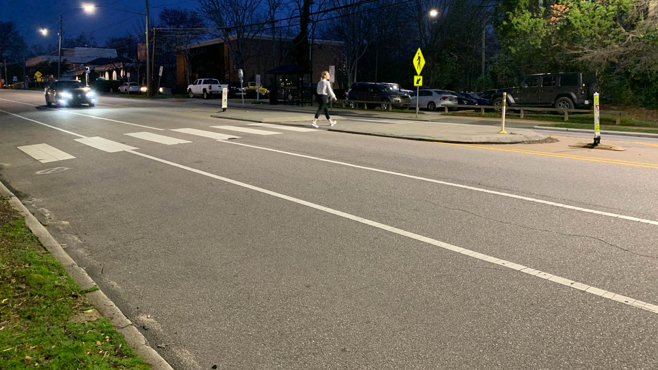 Woman crossing a midblock crosswalk to a pedestrian refuge island in the median at night. A car approaches the crosswalk.