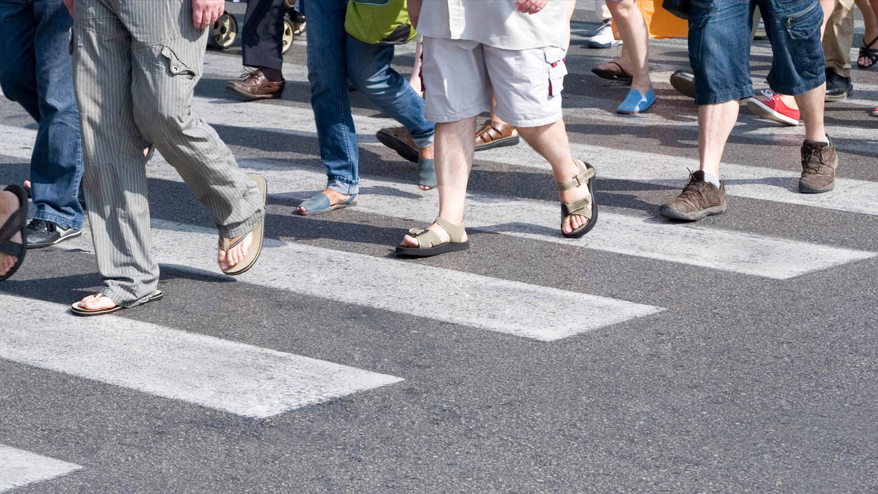 Photo of a tight close up shot of several pedestrian feet walking across a crosswalk.