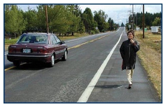 Photo of a pedestrian walking along the wide shoulder of a rural roadway.