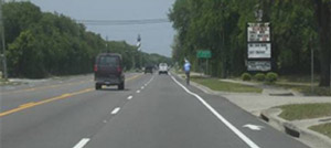 Photo.  A multi-lane high-speed roadway, with a wide bicycle lane on the far-right edge of the roadway, that is designated by an 8-inch longitudinal marking and arrow/symbol pavement markings.