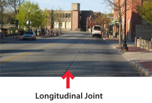 Photo.  An urban road with a longitudinal joint down the center of the travel lane.  The joint is located at the cold joint between pavement surfaces that may cause a cyclist to lose control and fall.