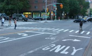 Photo.  An urban intersection with pavement markings on both the through and turn lanes to indicate proper placement for cyclists at the intersection.