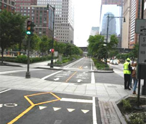 Photo.  An urban intersection between a shared use path and a street.  The two-lane shared use path has a separate signal for pedestrian and bicycle traffic to cross the intersection. However, pedestrian traffic on the sidewalk may conflict with the path movement. Traffic signs and pavement markings are used to direct traffic through the intersection and alert cyclists of crossing pedestrians, but the combined use of stop and yield lines may be confusing to approaching path users (the combined use of stop and yield lines does not conform to the MUTCD).