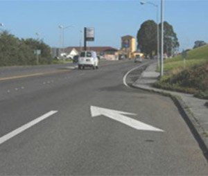 Photo.  A multilane roadway with an acceleration lane to the right and a bikeable shoulder beyond the merge point. Bicyclists have difficulty merging with higher-speed vehicle traffic at these locations because they are typically travelling at slower speeds and have a narrower profile.