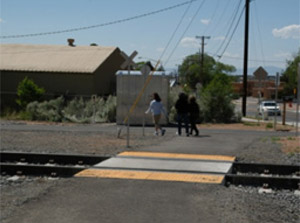 Photo.  A shared use path crossing a railroad track. There are bright yellow transitions on either side of the tracks and a concrete section in the middle of the tracks to create a smoother path.  Trains in the area are infrequent and pass through the corridor at low speeds.