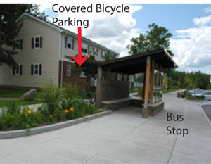 Photo.  Covered bicycle parking conveniently located behind a bus stop, with wide paths leading to the stop. Bicycle parking should be located as close to the activity as possible without impeding or conflicting with other users.
