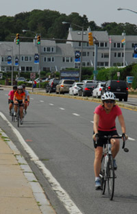 Photo.  Image of a four cyclists along a divided four-lane road with a traffic signal to their rear.