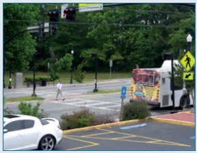 A mid-block PHB assists a pedestrian to cross a wide, busy arterial roadway to access a transit stop.