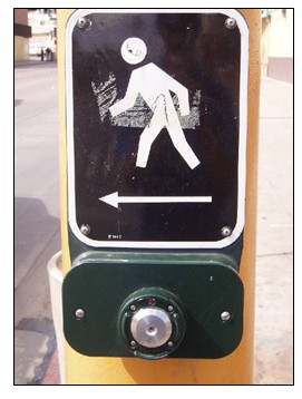 Photo of a call button that lights up when pressed. A plaque with an image of a pedestrian is above the call button.
