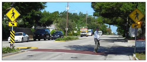 Photo of a pedestrian crosswalk with rectangual rapid flashing beacons and pedestrian warning signs mounted to posts on both ends of the crosswalk as well as on the median.