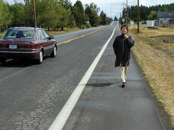 Woman walking on paved shoulder of two-lane road