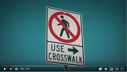 Screenshot of video shows a no pedestrians sign that underneath reads Use Crosswalk and has an arrow pointing right.