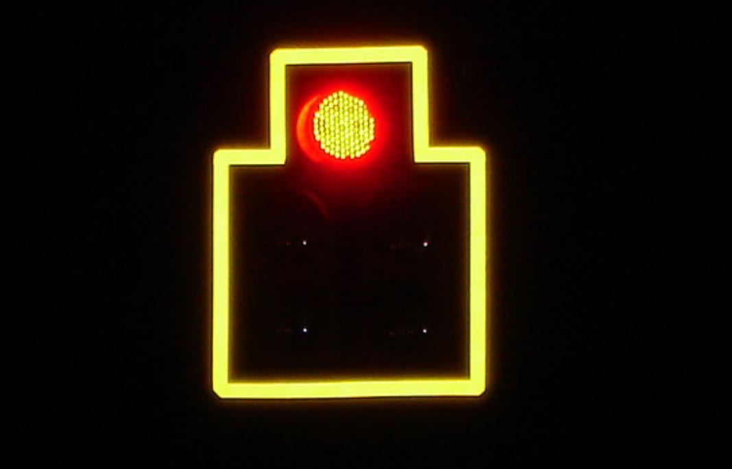 Photo: This nighttime photograph shows a traffic signal showing RED. While the traffic signal itself is not visible, a yellow retroreflective border is visible, outlining the border of the signal.