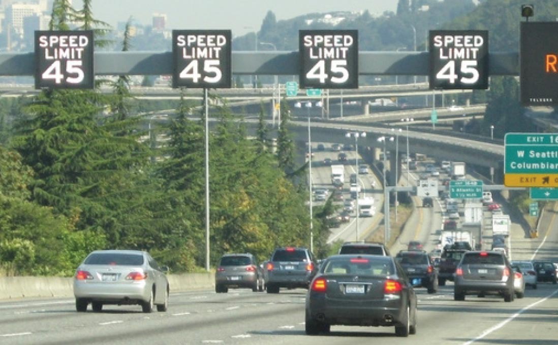 Photo: This photograph, taken from the edge of the freeway, shows four freeway lanes in the same direction. Over each travel lane is a variable speed limit sign reading SPEED LIMIT 45. To the right of the overhead variable speed limit signs is the left edge of an overhead variable message board sign. Three of the four travel lanes are congested, except for a restricted travel lane on the left.