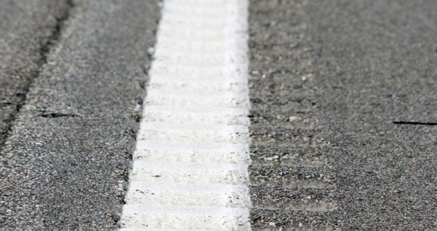 This photograph, taken along the edge line of a roadway, shows longitudinal rumble strips overlapping with the edge line of the roadway.