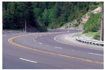 Photo of a curvy, relatively horizontal 4-lane road in the shape of an S as it winds along the outline of a mountainside.