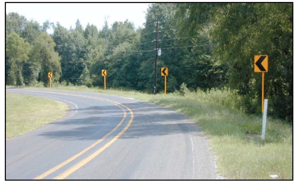 Photograph of a two-lane roadway with edge lines and centerlines in a rural area. Four chevrons are installed on the outside of the curve.