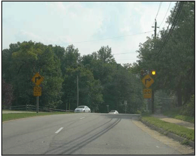 Photograph showing a typical arrangement of a horizontal alignment sign and a flashing beacon. A horizontal alignment sign with an advisory speed plaque is installed on both sides of a four-lane roadway. One is on the shoulder and the other one is on the median. The flashing beacons are installed on the top of the advance horizontal alignment signs.