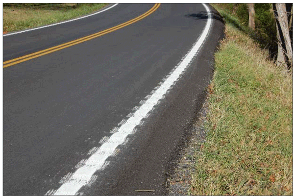 Close-up photograph of milled edge line rumble strips. The rumble strips are milled over the edge line of a two-lane roadway within a curved section.