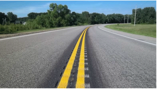 Close-up photograph of centerline rumble strips. It is a two-lane roadway located in a rural area. The rumble strips are milled into the surface underneath the centerline.