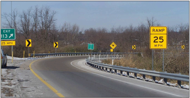 Photograph of a one-lane ramp with guardrails along inside and outside of the curve. In addition to the guardrails, chevrons are installed on the outside of the curve. An advisory speed sign is installed prior to the curve.