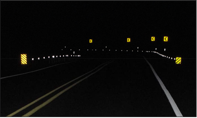 Photograph of a nighttime view of delineators installed on post. Guardrails are installed on the inside and outside of a horizontal curve on a two-lane roadway. Delineators are installed on posts. The retroreflective delineators provide better visibility during the nighttime.