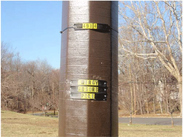 A close-up photograph of the energy absorbing utility pole. On the pole, there are tags showing the 4-digit pole number and a label read as "Energy Absorb Pole".