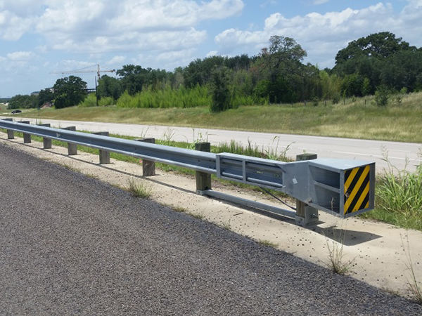 Figure 2.  Photo.  Example of a barrier terminal.  This photo shows a barrier terminal installed on the side of an asphalt road. The black and yellow warning stripes indicate the end of the barrier.