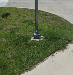 Figure 4.  Photo.  Example of breakaway hardware.  This photo shows the base of a sign pole on a street corner. The pole has breakaway hardware installed at the bottom.