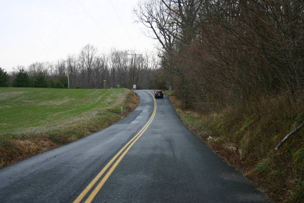 Photo. A car traveling on a two-lane road with a double yellow centerline.