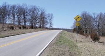 Photo.  Photo shows an advance curve warning sign with an advisory speed plaque of 45 mph on an approach to a horizontal curve.