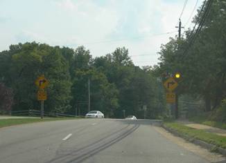Photo.  The photo shows a curve on a four-lane, median-divided roadway with two horizontal alignment signs with advisory speed plaques- one on each side of the road.  The sign on the right has flashing beacons on top of the sign to help with visibility.  The flashing beacons consist of two yellow LEDs placed on either side of the sign which flash alternately.