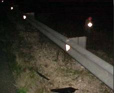 Photo.   Photo shows installation of reflectors on a metal guardrail.  This photo is a view approaching the guardrail at an angle.